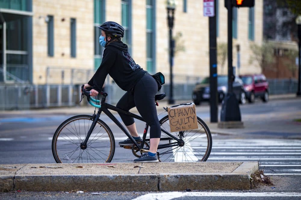 A cyclist stopped at a red light at Malcolm X. Boulevard in Nubian Square in Roxbury with a sign reading “CHAUVIN GUILTY ON ALL 3.” (Jesse Costa/WBUR)