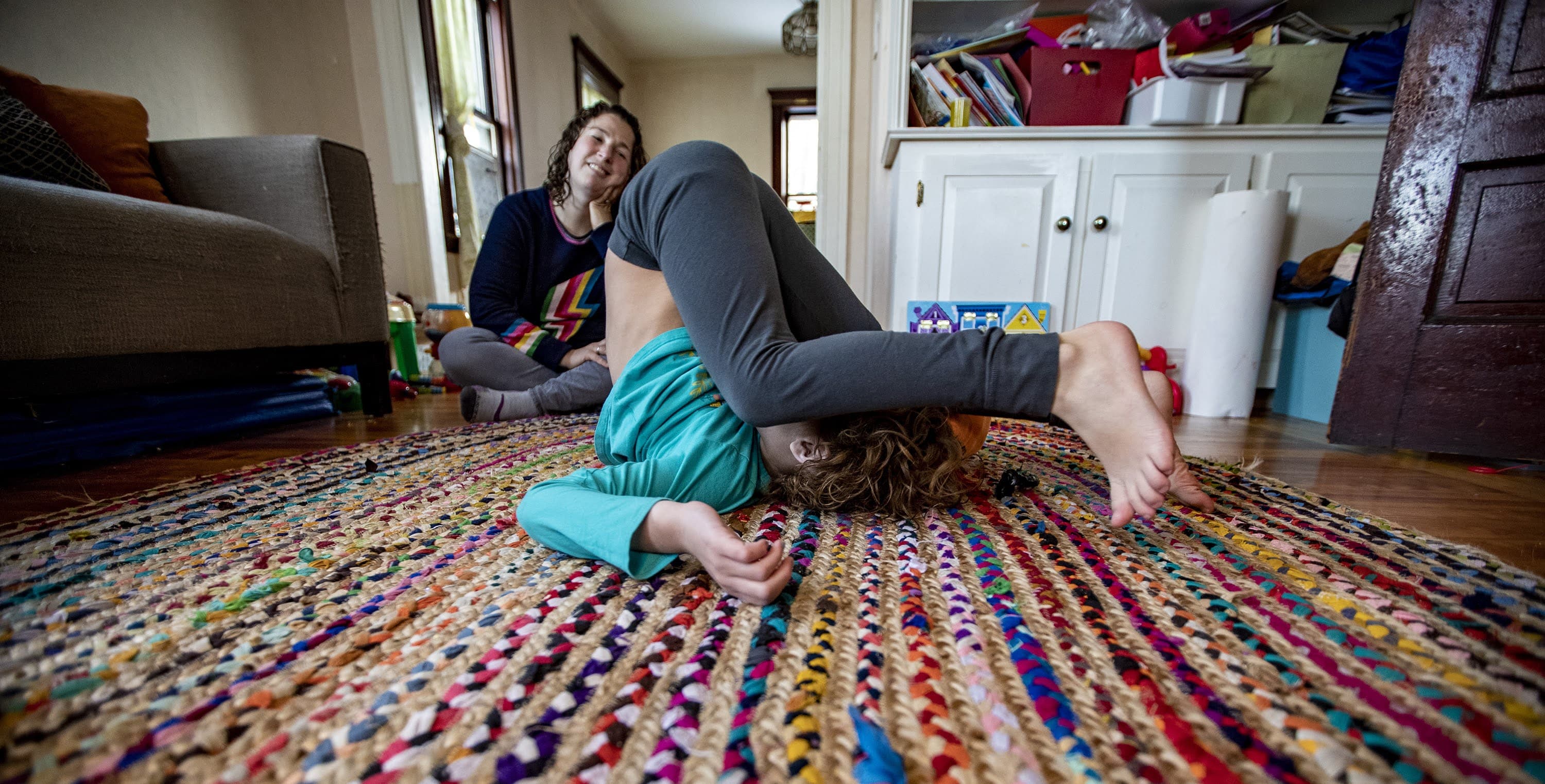 Hallel does a backwards roll in the living room as their mother watches. (Jesse Costa/WBUR)