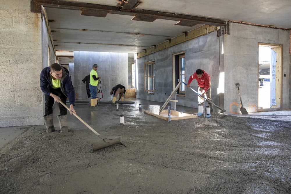 Construction workers spread concrete over a thick layer of insulation to form the ground floor of one of the new passive house buildings at the Hillside Center for Sustainable Living in Newburyport, Mass. (Robin Lubbock/WBUR)