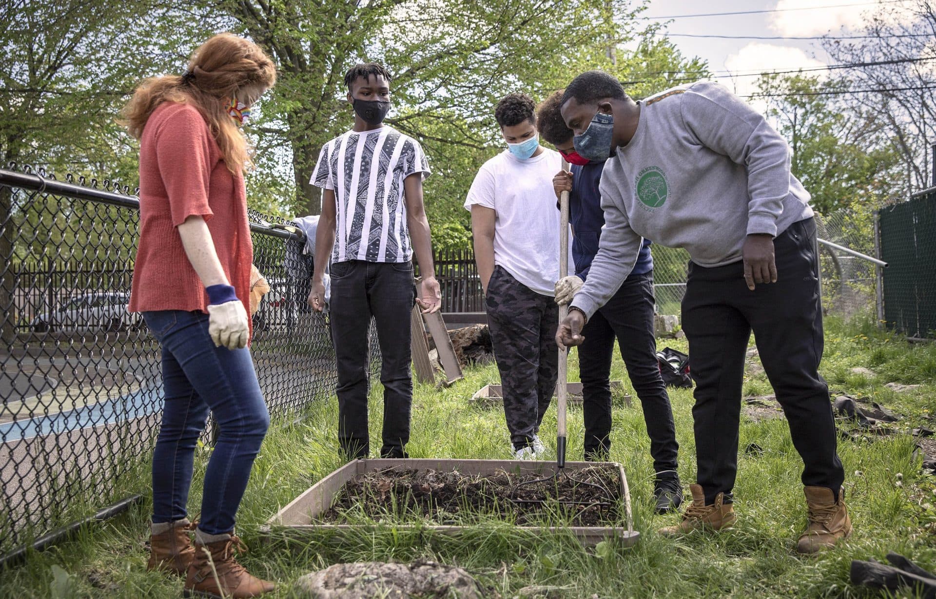 Teachers Rebekah Shyloski and Deric Quest gather with students around a raised bed outside the Greenwood School in Dorchester. (Robin Lubbock/WBUR)