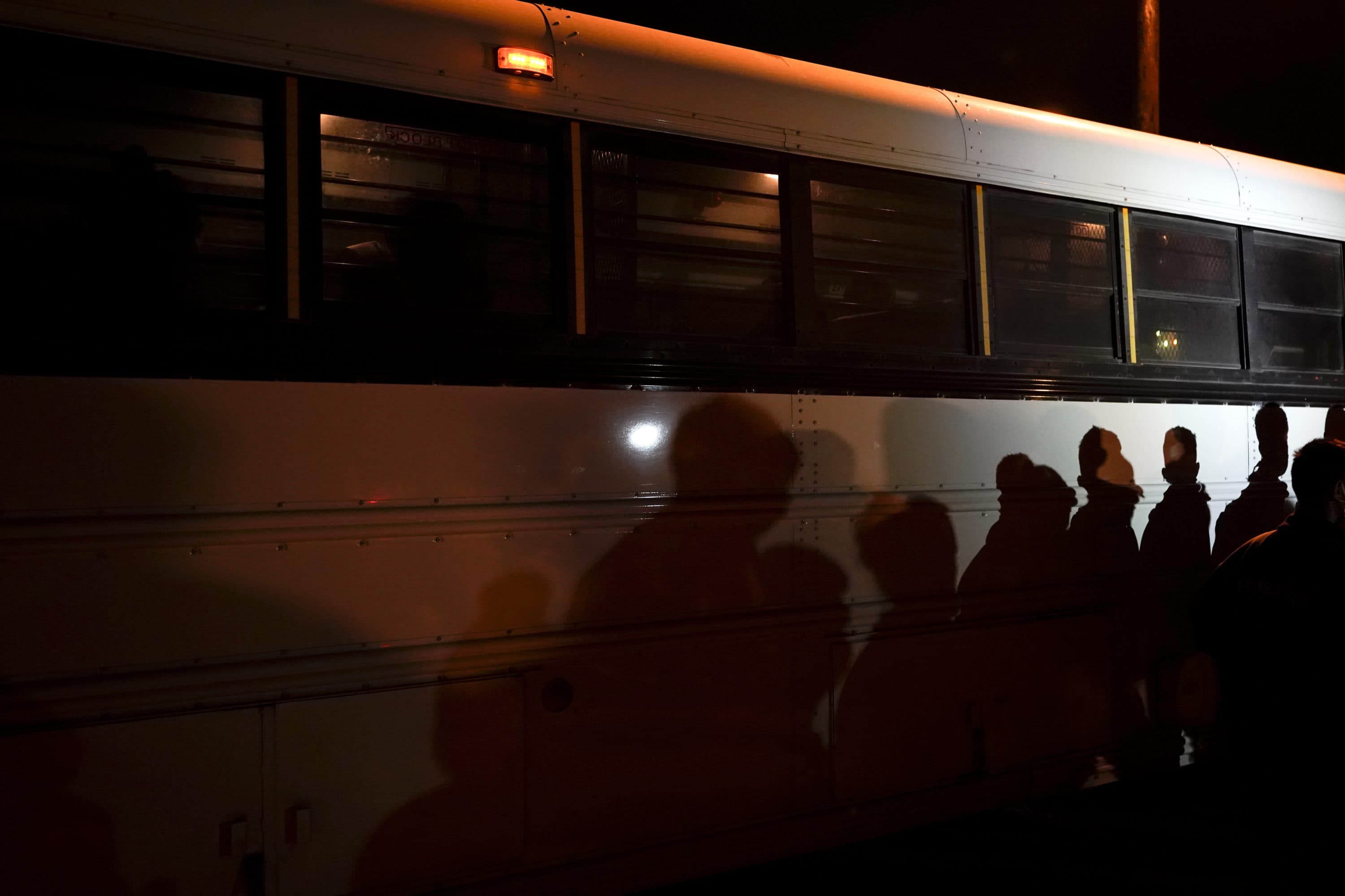 Shadows of migrants lined up at an intake area are cast along the side of a bus after turning themselves in upon crossing the U.S.-Mexico border in Roma, Texas, May 11, 2021. (Gregory Bull/AP)
