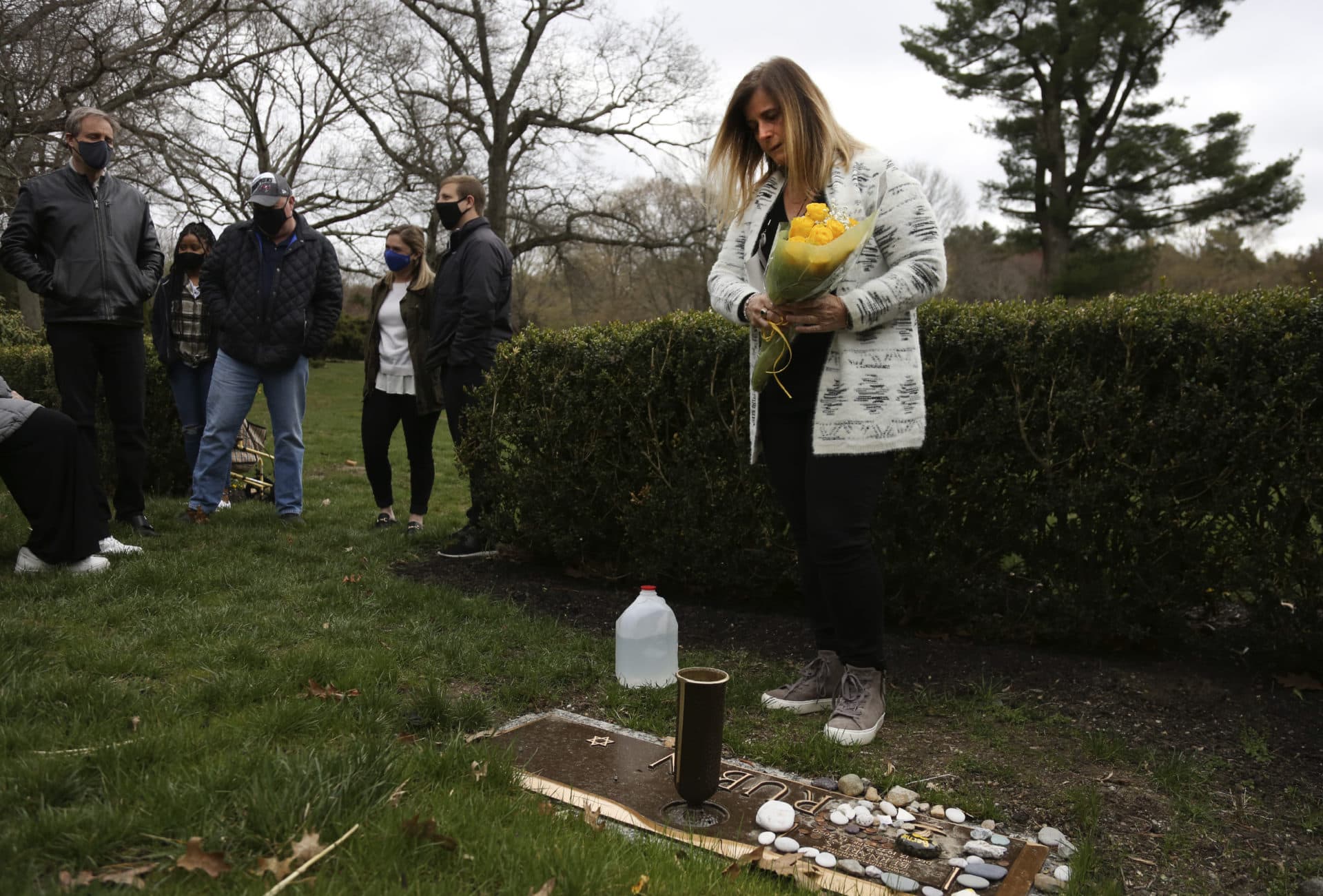 Michelle Pepe places a bouquet of yellow roses on her father's grave as family and friends watch in Sharon, Mass., on Tuesday, April 13, 2021.  (Jessie Wardarski/AP)