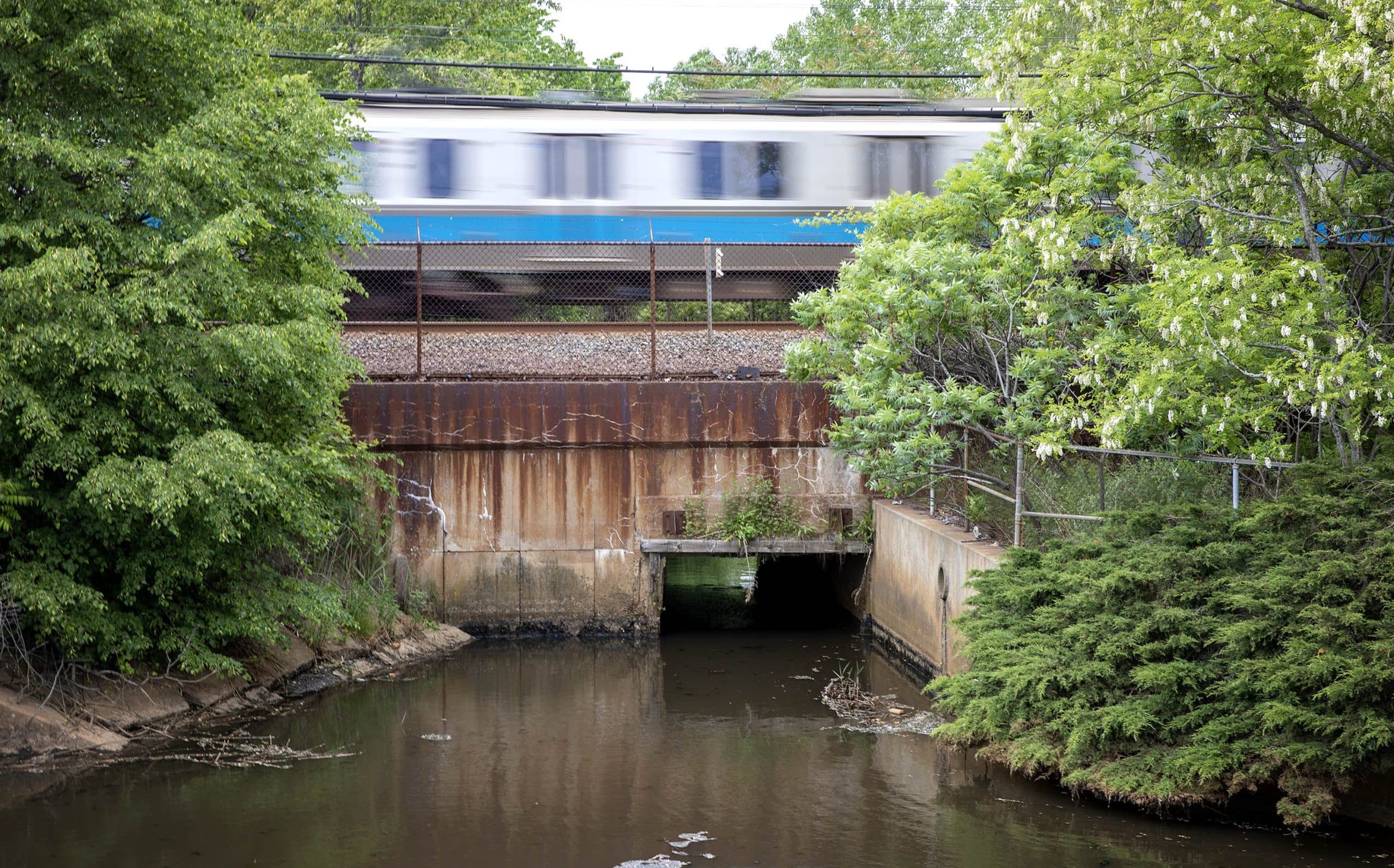 A Blue Line train passes over a culvert next to the DCR Bennington Street Pump Station. Water from Suffolk Downs flows through the culvert into this pond. Water flowing in the opposite direction, from Belle Isle Marsh, is blocked by tide gates. (Robin Lubbock/WBUR)