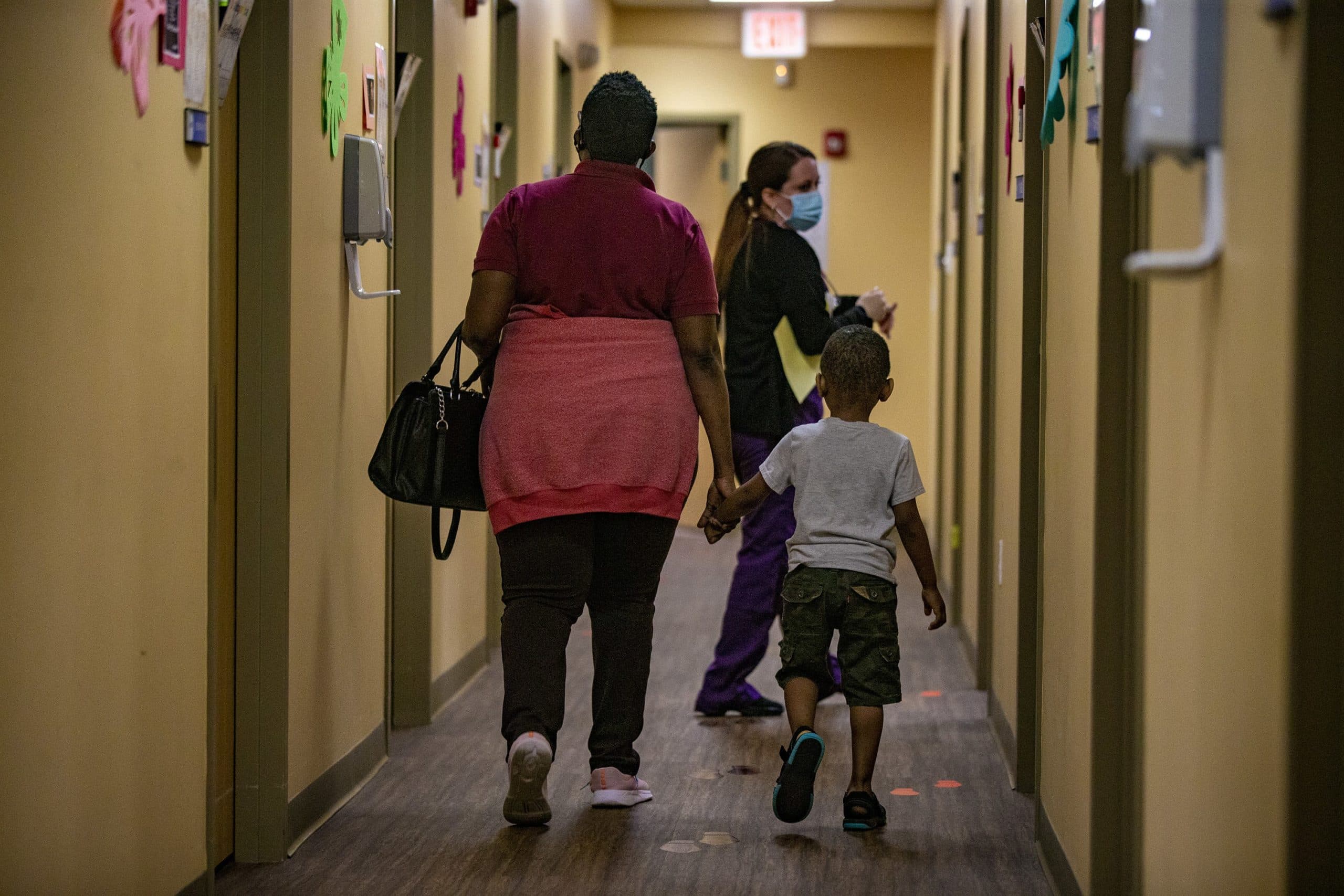 Medical assistant Keyla Santiago-Rivera leads a mother and child to an examination room at Brockton Neighborhood Health Center. (Jesse Costa/WBUR)