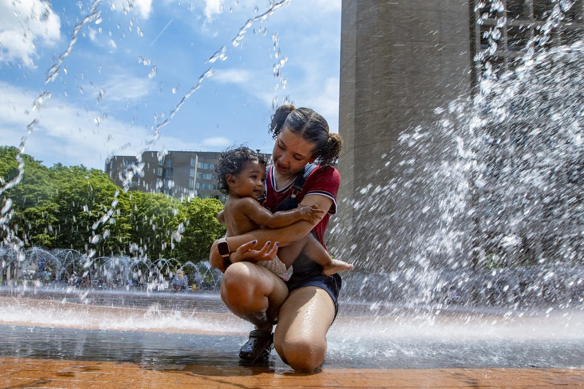 Adiana Hollis, 14, holds 14-month-old Julian Mel in her arms while they cool off in the fountain at the Christian Science Plaza. (Jesse Costa/WBUR)