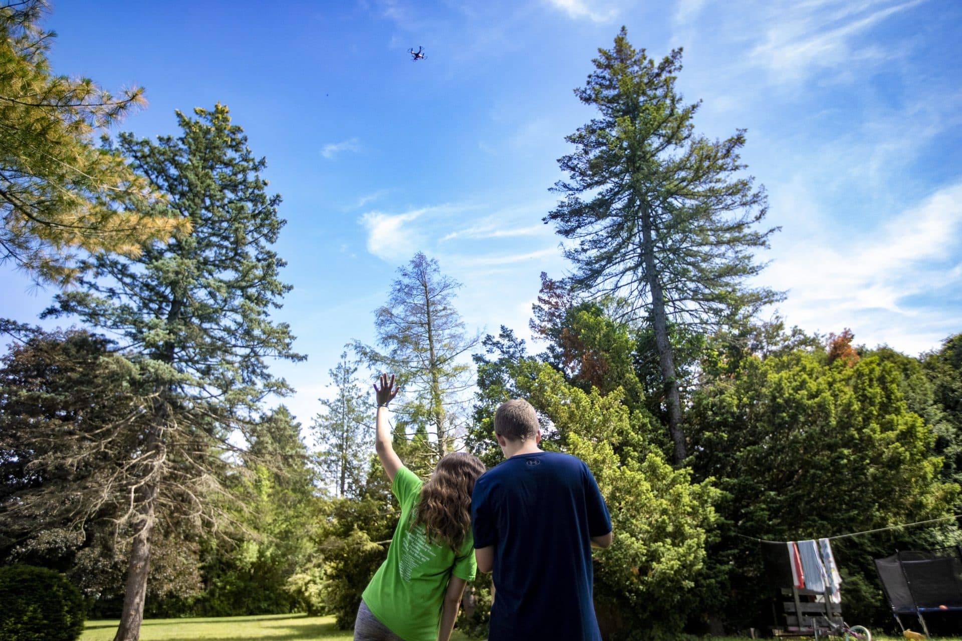 Emily, 13, waves at the drone that her brother Charlie, 12, is flying high above their heads in the backyard of their home in West Springfield. (Jesse Costa/WBUR)