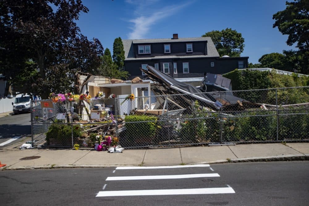 Flowers left outside a fence surrounding a building that was destroyed, authorities say, by the driver of a stolen plumbing company truck. The suspect then shot and killed U.S. Air Force veteran Ramona Cooper and retired Massachusetts State Police trooper David Green. (Jesse Costa/WBUR)
