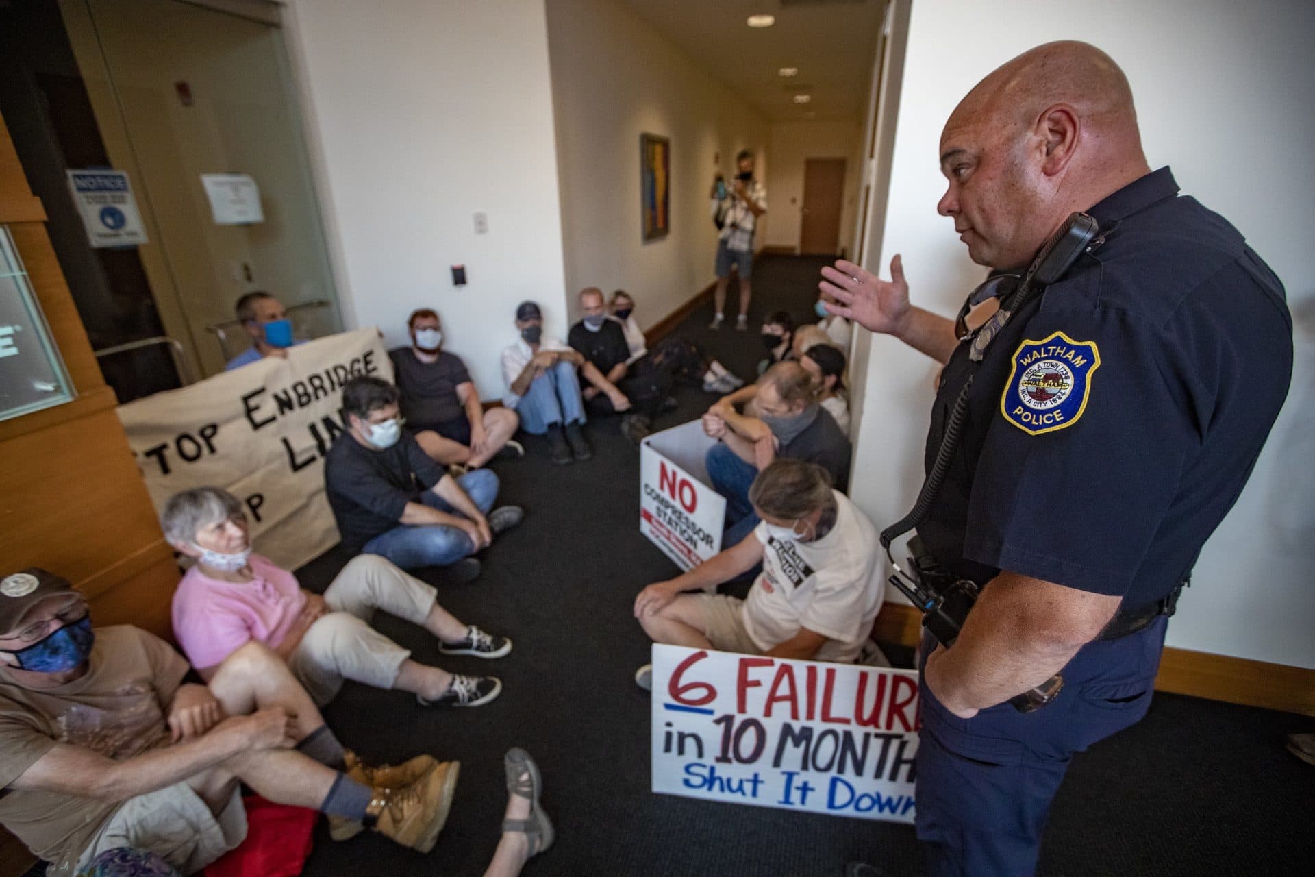 A Waltham police officer speaks with the protesters at the Enbridge office. (Jesse Costa/WBUR)