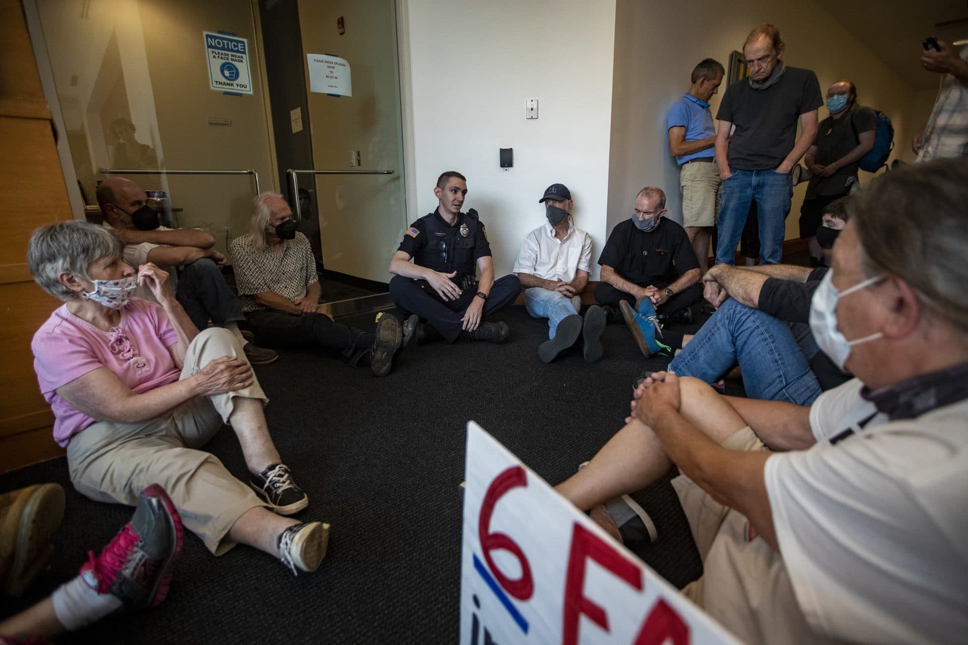 A Waltham police officer sits with protesters to tell them they are trespassing. (Jesse Costa/WBUR)