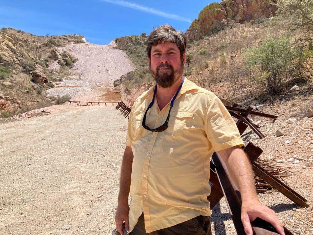 Myles Traphagen of the Wildlands Network pictured in front of a mountaintop blown up to make way for the border wall — unfinished and unsecured. (Peter O'Dowd/Here &amp; Now)