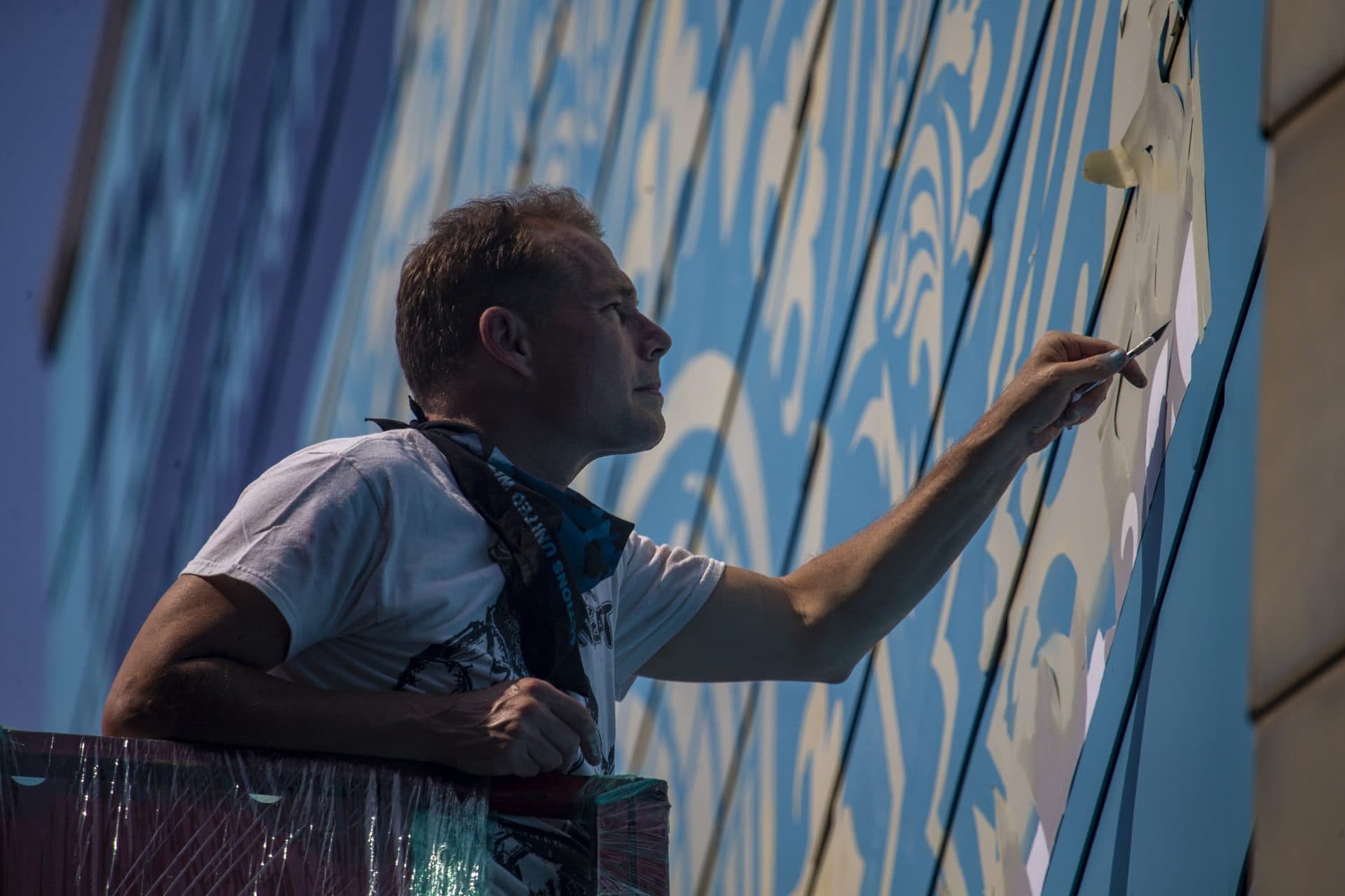 Shepard Fairy cuts out the stencil for the mural being installed on a wall of the IMAX Simon’s Theater at the New England Aquarium. The mural is part of Sea Walls, an environmental public art project based in East Boston to raise awareness about the effects of climate change on the planet's fragile oceans. (Jesse Costa/WBUR)