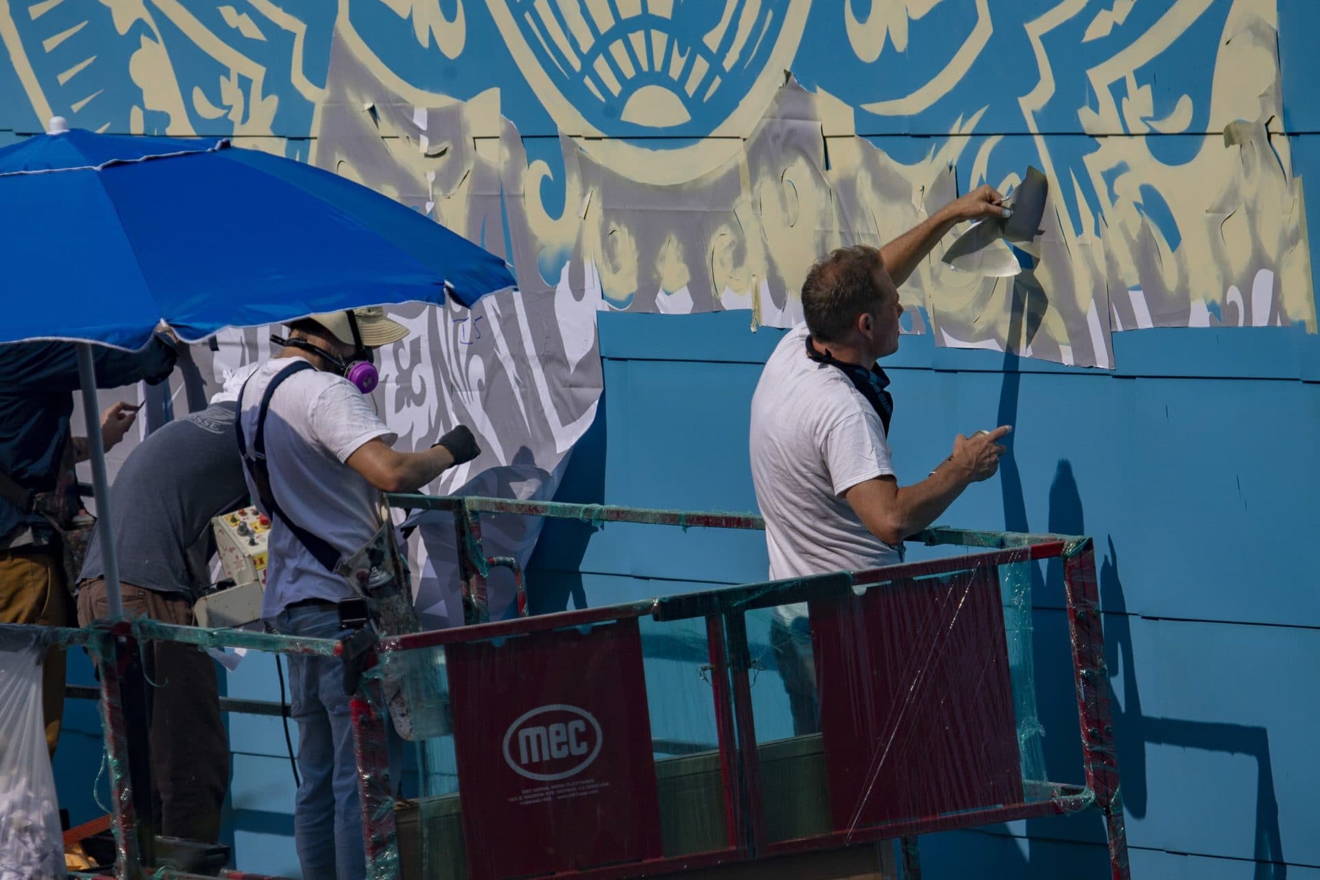 Shepard Fairy pulls away part of the stencil for the mural being installed on a wall of the IMAX Simon’s Theater at the New England Aquarium. (Jesse Costa/WBUR)