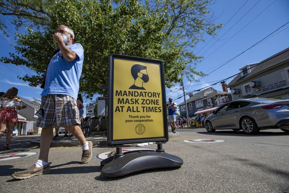 A man adjusts his mask as he walks across Commercial Street in Provincetown. (Jesse Costa/WBUR)