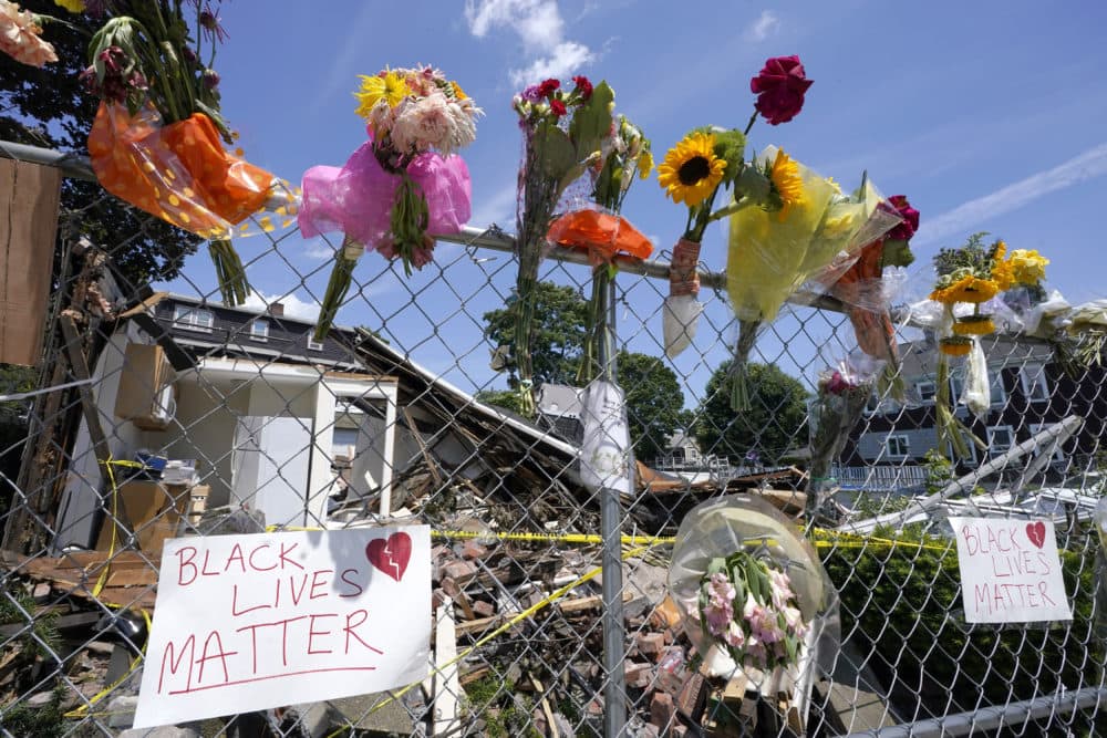 Signs and flowers are attached to a fence outside a building in Winthrop, Mass., on Monday, June 28, 2021, where an armed man crashed a hijacked truck, Saturday, June 26, 2021, then fatally shot two people before being killed by police. (Steven Senne/AP)