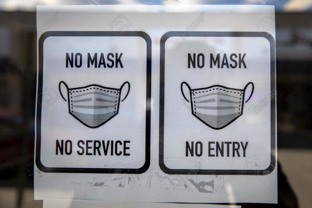 A sign requiring customers to wear masks is displayed on the door at Cash Point in Medford Square. (Robin Lubbock/WBUR)
