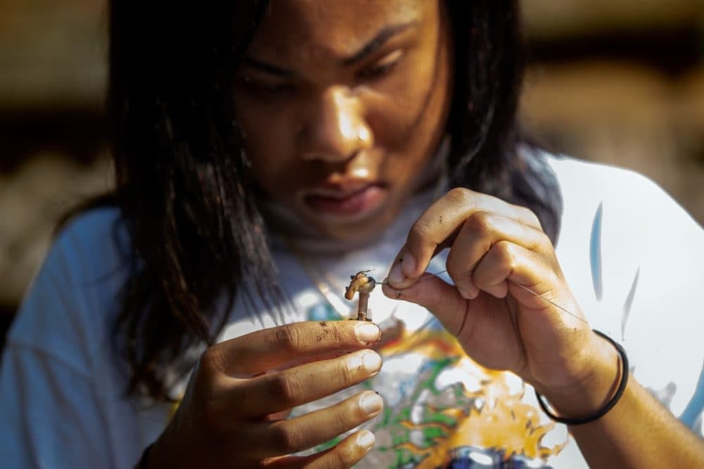 Alaysia Mondon, 14, baits her hook with a worm while fishing on Lake Lashaway. (Jesse Costa/WBUR)