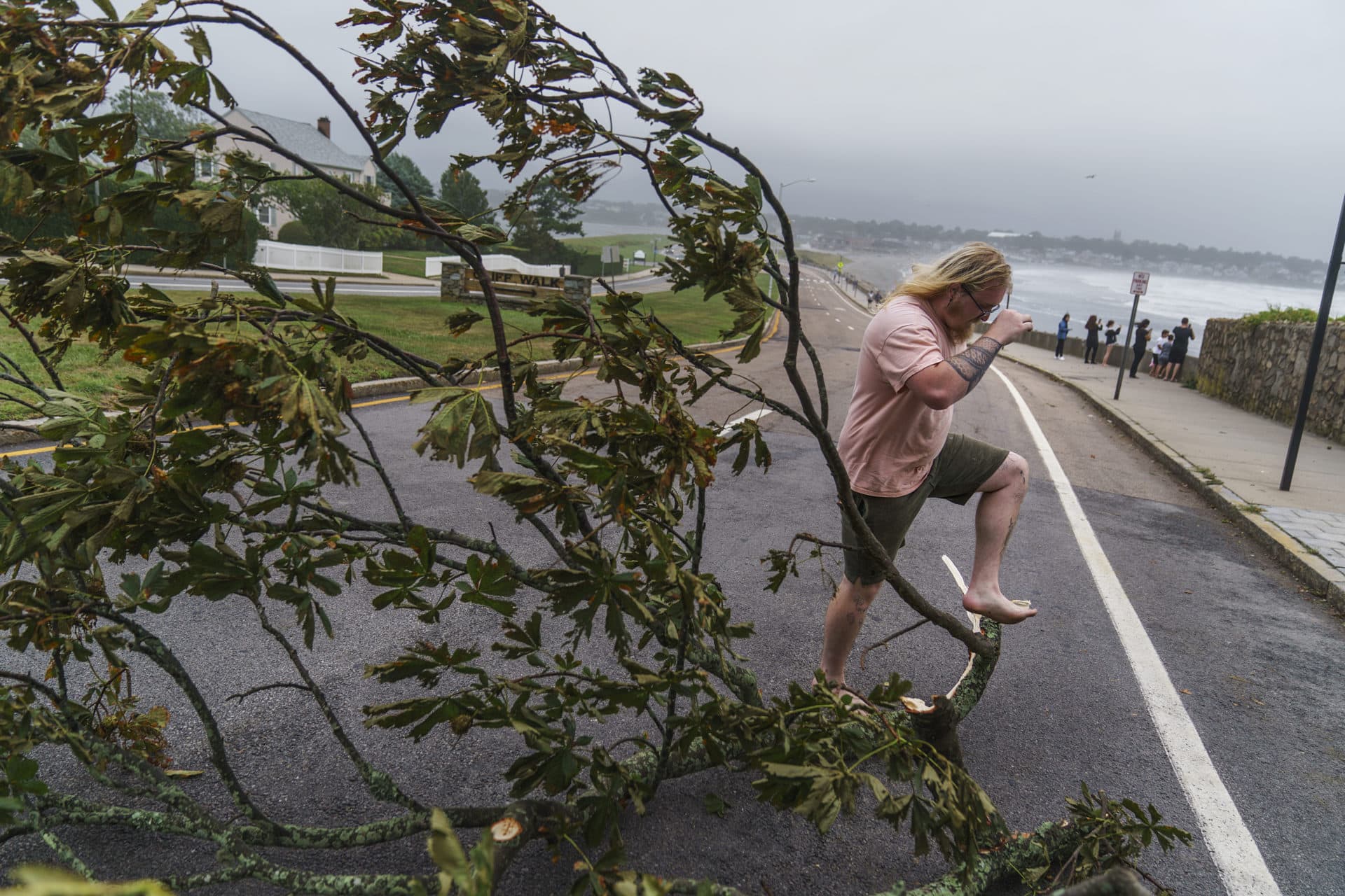 Zeke Baker steps over a fallen tree branch while clearing debris from a sidewalk in Newport, R.I. (David Goldman/AP)