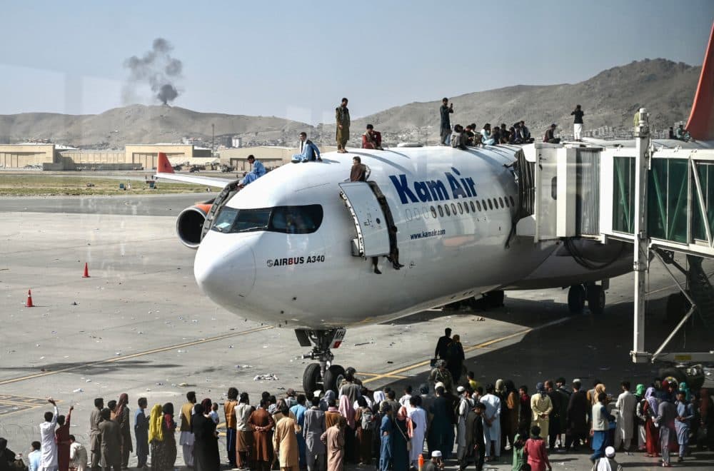 Afghan people climb atop a plane as they wait at the Kabul airport in Kabul on Aug. 16, 2021. (Wakil Kohsar/AFP via Getty Images)