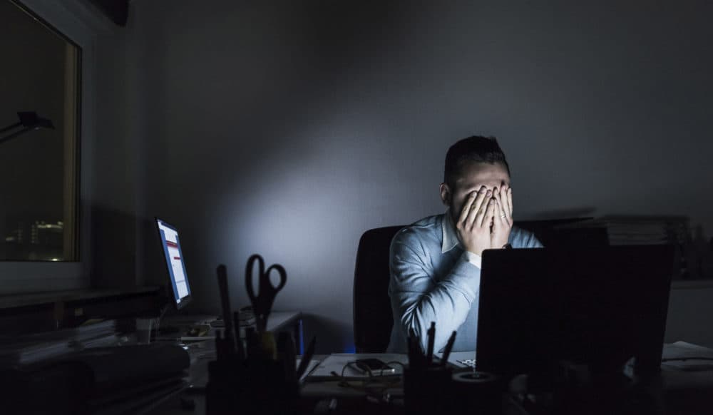Exhausted businessman sitting at desk in office at night (Getty Images)