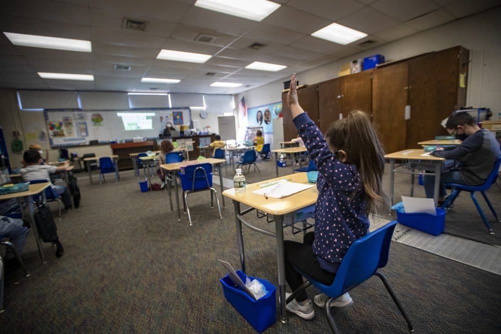 A student at Barbieri Elementary School in Framingham raises her hand in March of 2021. All children in public schools in Massachusetts must wear a mask until Nov. 1, under a state mandate. (Jesse Costa/WBUR)