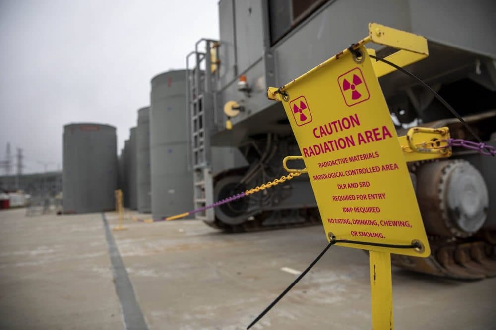 A sign by casks containing spent fuel on a concrete pad near the Pilgrim reactor building, warns of the presence of radioactive materials. (Robin Lubbock/WBUR)