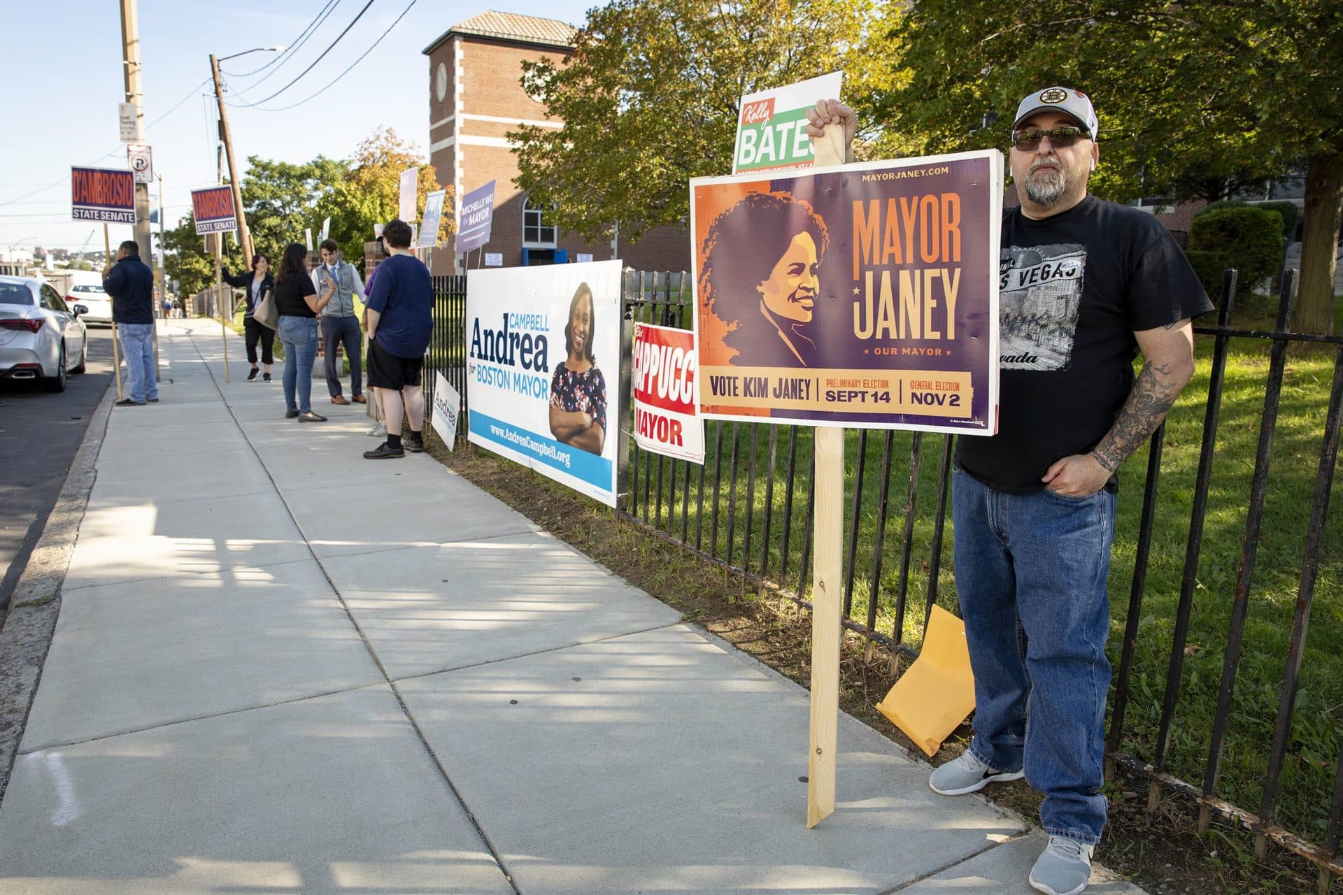 Larry Tinnirello holds up a &quot;vote Kim Janey&quot; sign outside the East Boston High School polling station. (Robin Lubbock/WBUR)