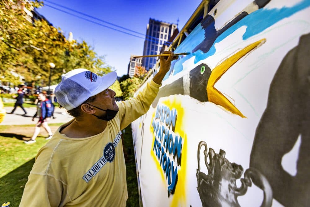 Robert Peters paints part of a mural illustrating Indigenous history in the Boston Marathon near the finish line in Copley Square. (Jesse Costa/WBUR)