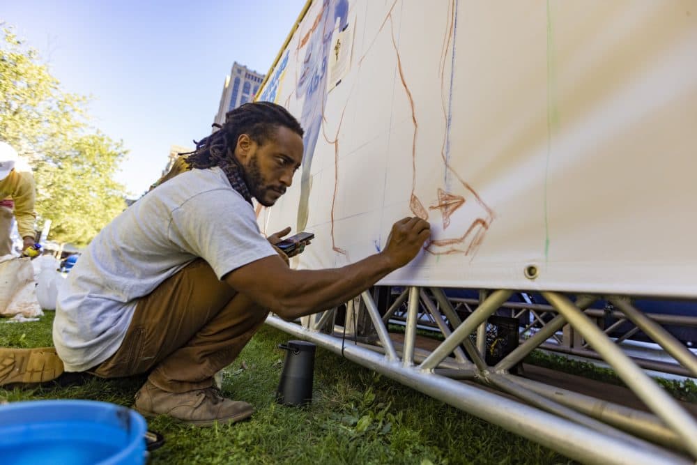 Robert Peters Jr. draws the outline of what will become the image of Ellison Brown, one of two Native Americans ever to win the Boston Marathon, near the finish line in Copley Square. (Jesse Costa/WBUR)