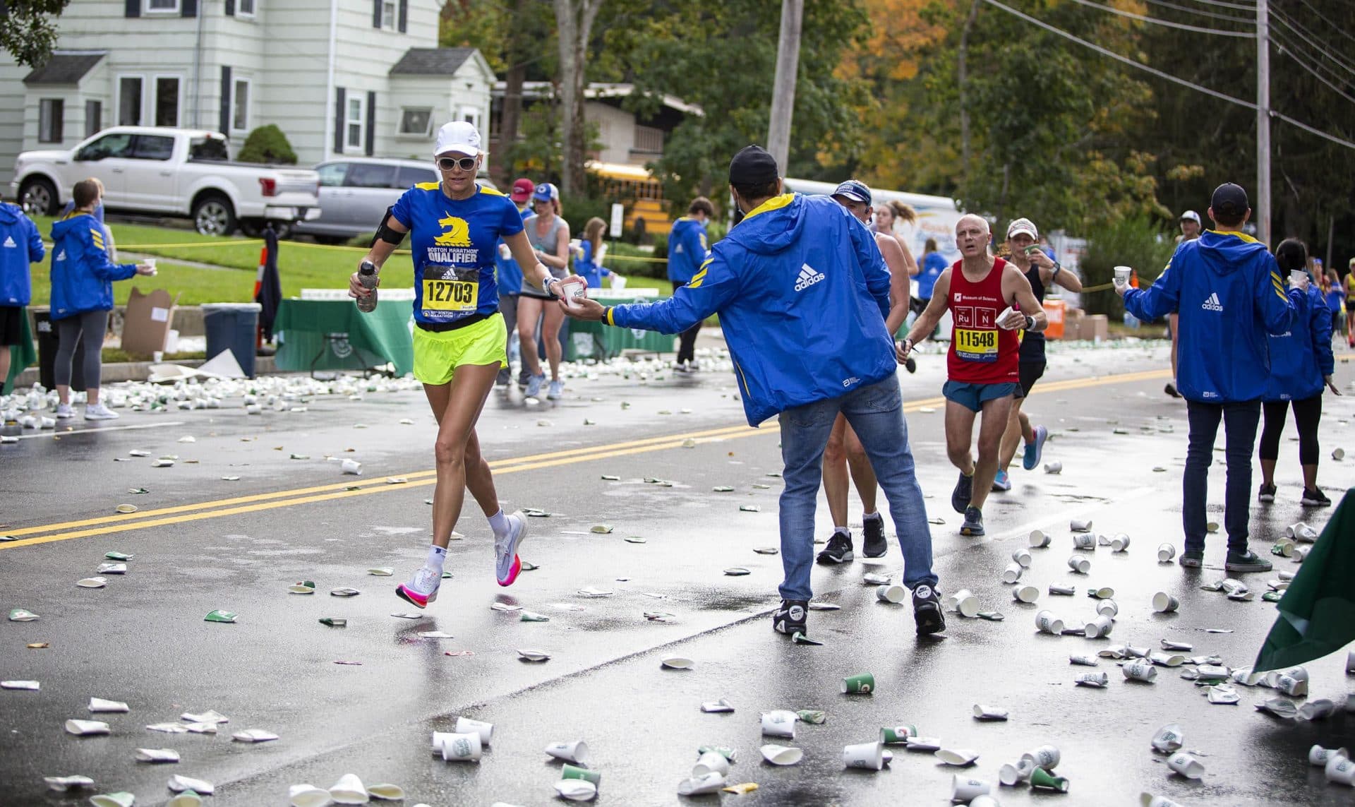 A runner takes a water cup from a volunteer at a marathon route water station in Newton. (Robin Lubbock/WBUR)