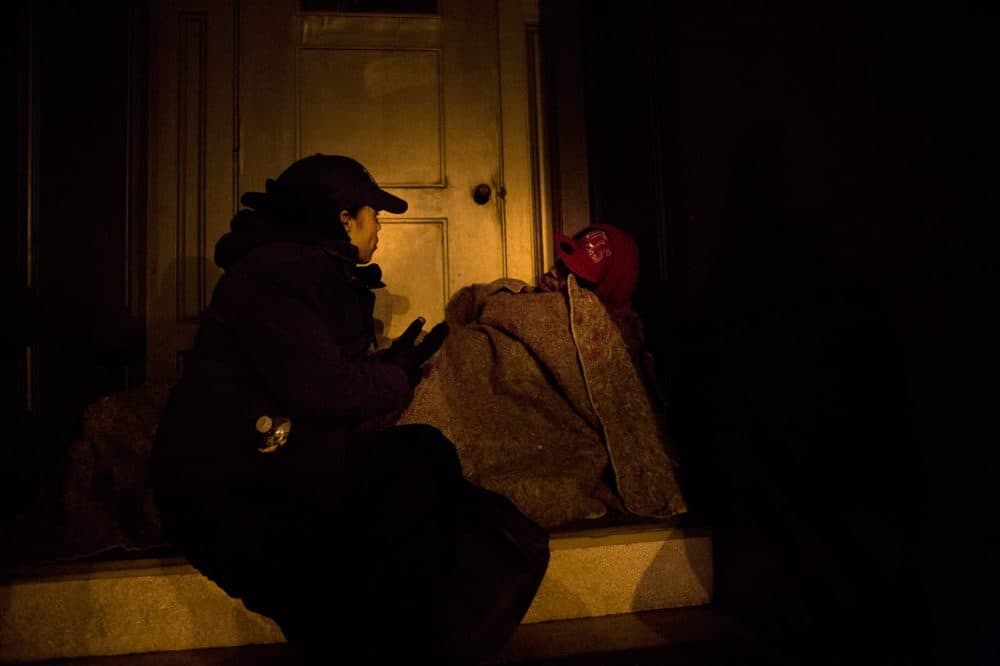 Elisabeth Jackson, executive director of Bridge Over Troubled Waters, asks a homeless person sleeping in a doorway on Bromfield St. if he needs any assistance during Boston's annual homeless census in 2013. (Jesse Costa/WBUR)
