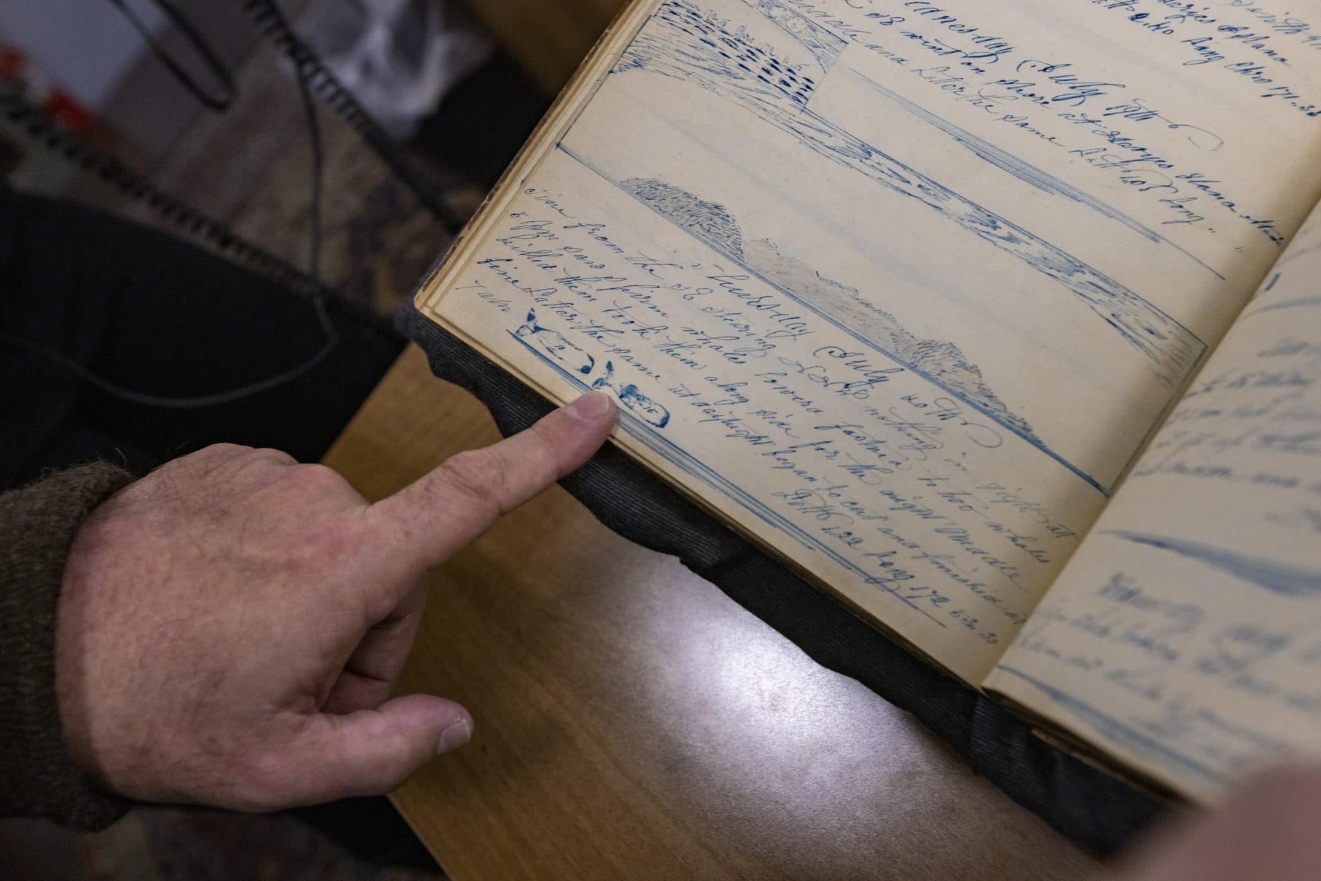 Some of the log books have intricate drawings of physical details, notes of things seen during the voyages of the ships. Here, Timothy Walker, history professor at UMass Darmouth, points out a day where the Ship Lion captured two whales which is marked by using a whale stamp. (Jesse Costa/WBUR)