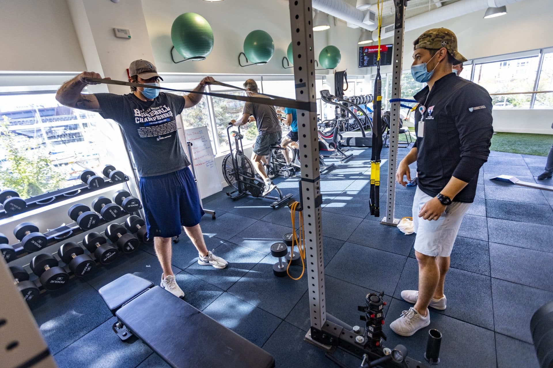 Athletic trainer and strength conditioning specialist Chris Manzano watches as Ryan Campbell does band exercises in the gym at Home Base in Charlestown. (Jesse Costa/WBUR)
