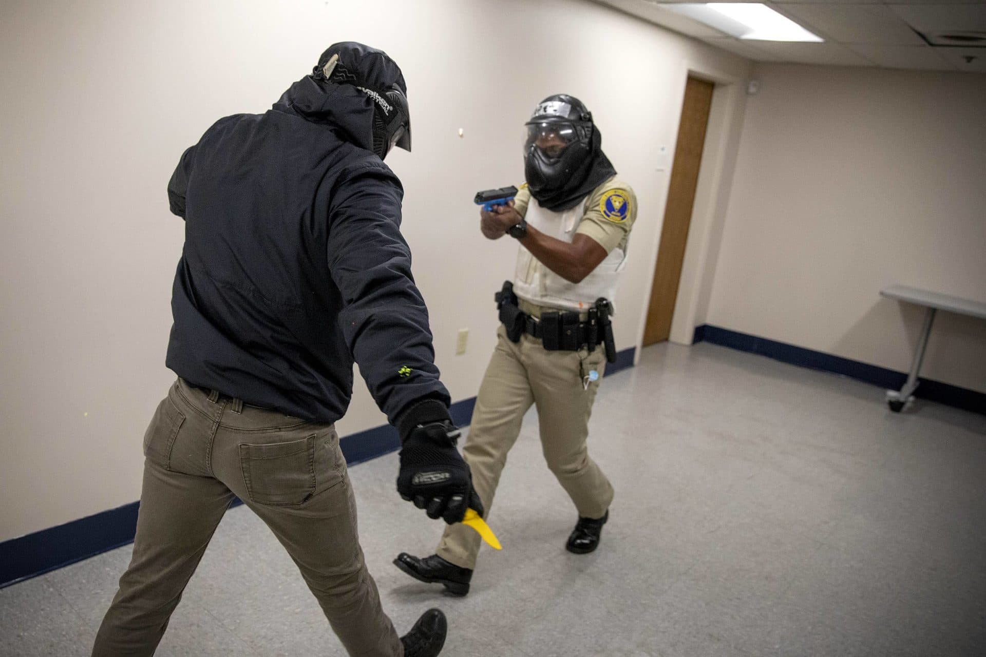At a police academy training session a student officer fires a paint gun as he backs away form an assailant pursuing him with a fake knife. (Robin Lubbock/WBUR)
