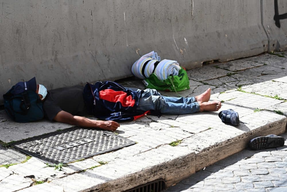 A homeless person wearing a protective mask lies asleep on the pavement in Rome's central Piazza Venezia on April 17, 2020. (Vincenzo Pinto/AFP via Getty Images)