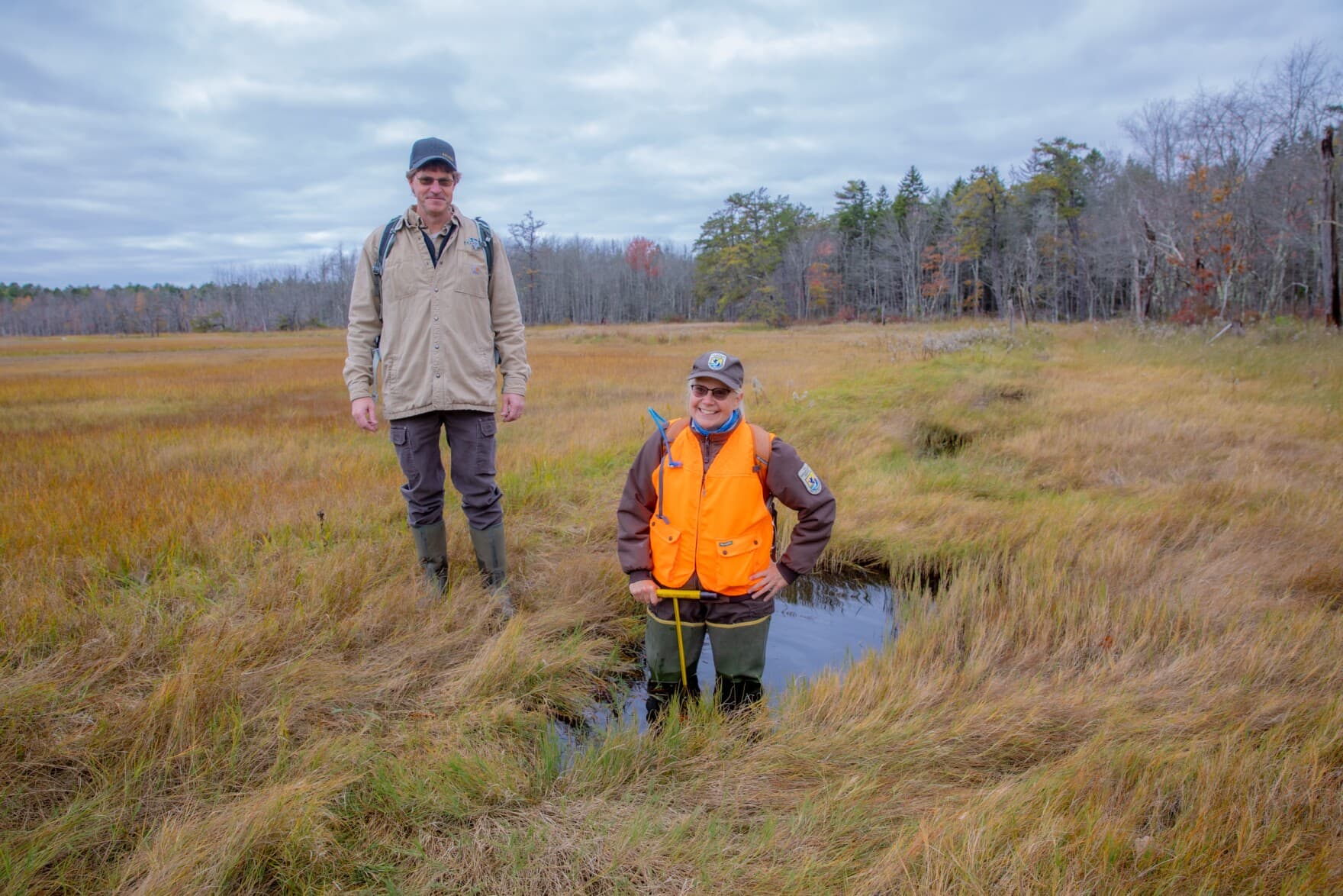 Geoff Wilson stands on an embankment, while Susan Adamowicz stands in a pool, or a 'borrow ditch' that farmers used to borrow soil to make embankments. (Rebecca Conley/Maine Public)