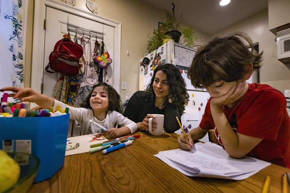 Mei Elensary watches her 4-year-old daughter, Mimi, reach for a marker, while her 9-year-old son, Amir, finishes a writing exercise before school. (Jesse Costa/WBUR)