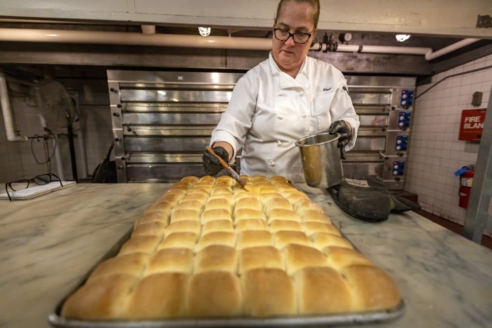 Omni Parker House baker Sheri Weisenberger brushes melted butter onto a pan of baked Parker House rolls. (Jesse Costa/WBUR)