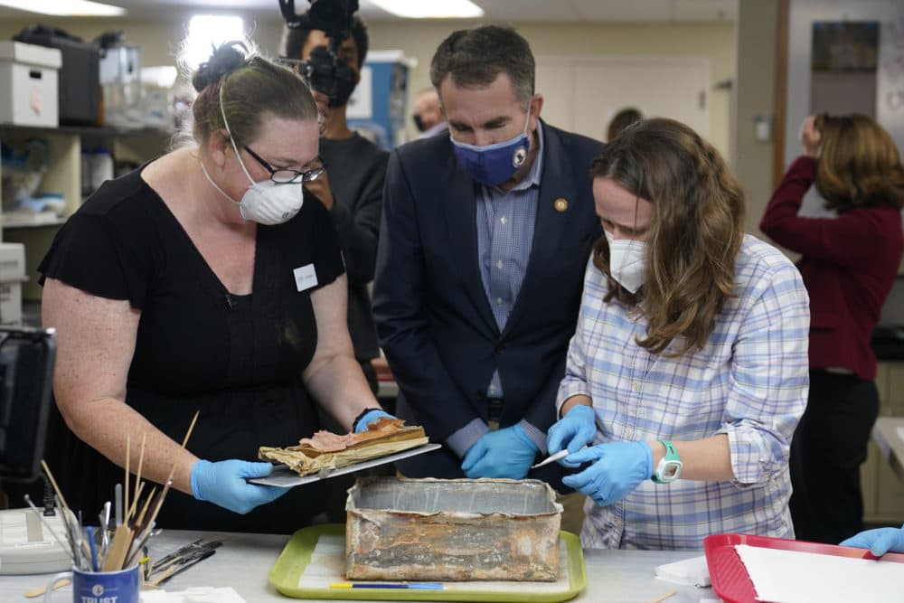 Virignia Gov. Ralph Northam, center, watches as lead conservator for the Virginia Department of Historic Resources, Kate Ridgway, left, and Sue Donovon, conservator for Special Collections for the University of Virginia, right, remove the contents of a time capsule that was removed from the pedestal that once held the statue of Confederate General Robert E. Lee on Monument Ave. Wednesday Dec. 22, 2021, in Richmond, Va. Three books and an envelope with a photo were inside the box. (Steve Helber/AP)