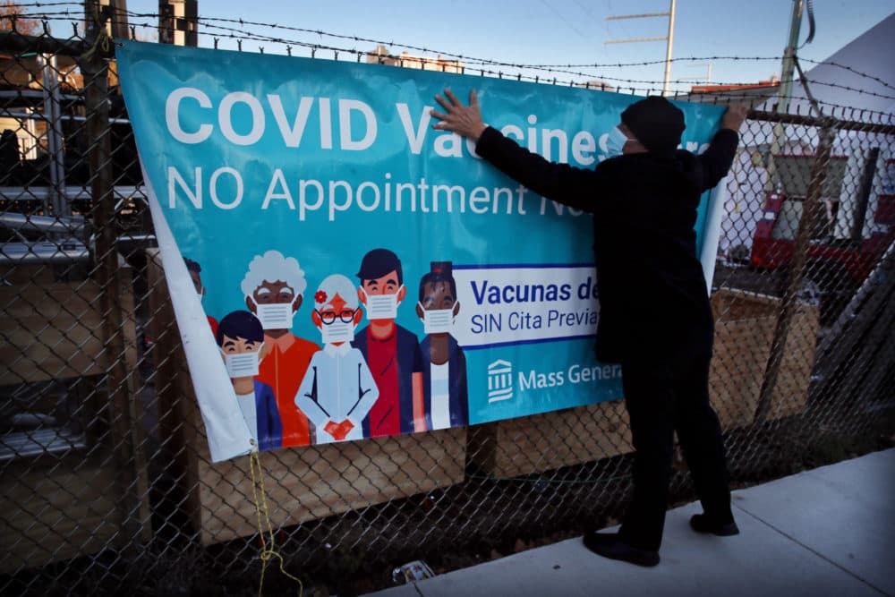 Oswald Gil hangs a COVID Vaccine banner on a fence during a Thanksgiving party at La Colaborativa in Chelsea, MA on November 23, 2021. La Colaborativa held a Thanksgiving party with prizes for young kids, free food boxes for families, and more, to entice them to vaccinate their youngsters. (Craig F. Walker/The Boston Globe via Getty Images)