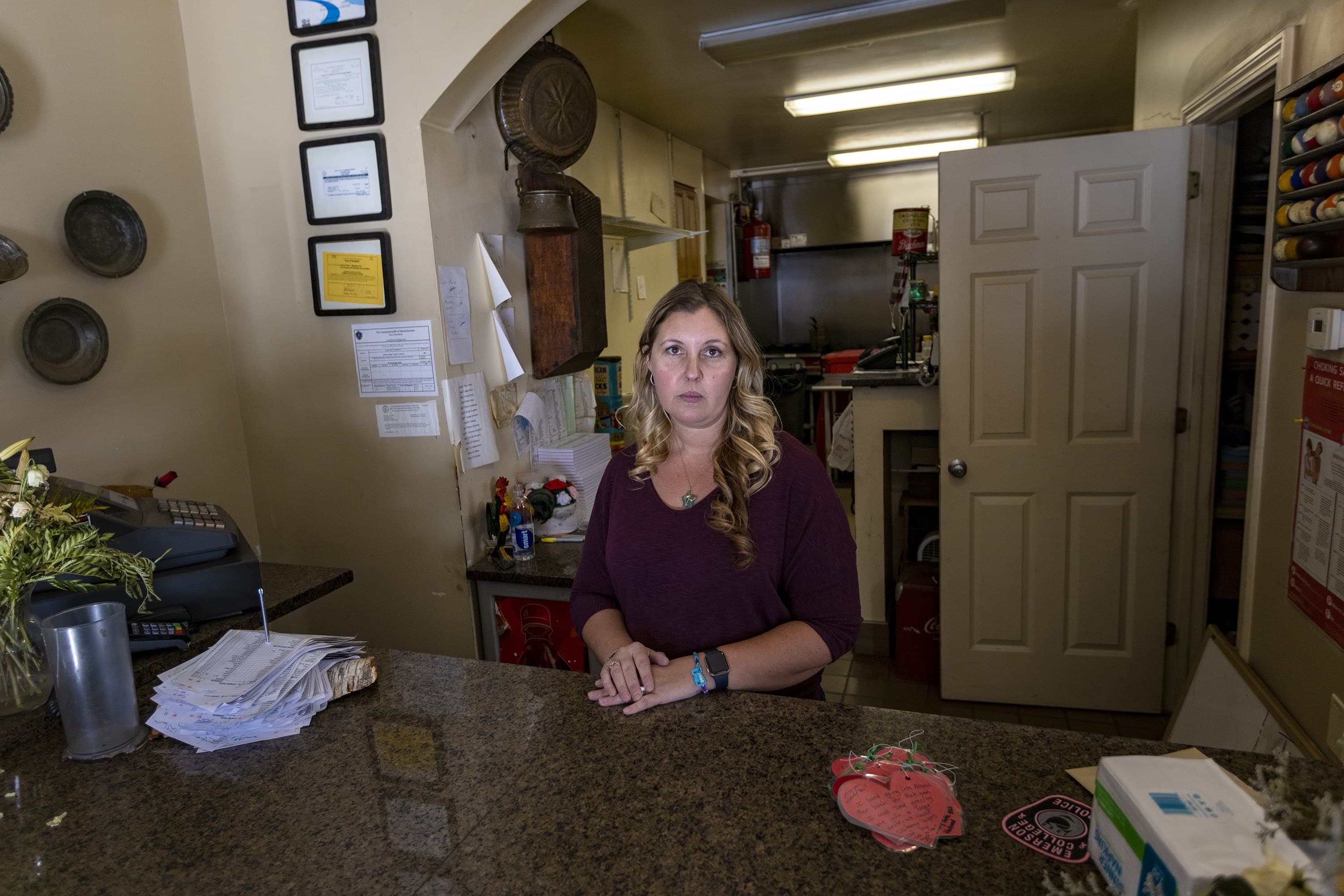 Rona Tsantinis-Roy stands behind the counter at Athens Pizza, a pizza shop in Brimfield her father owned for many years. Tsantinis-Roy‘s father Tony Tsantinis died of COVID-19 last month, when efforts to find space at a hospital that could offer him a higher level of care to treat him could not be found. (Jesse Costa/WBUR)