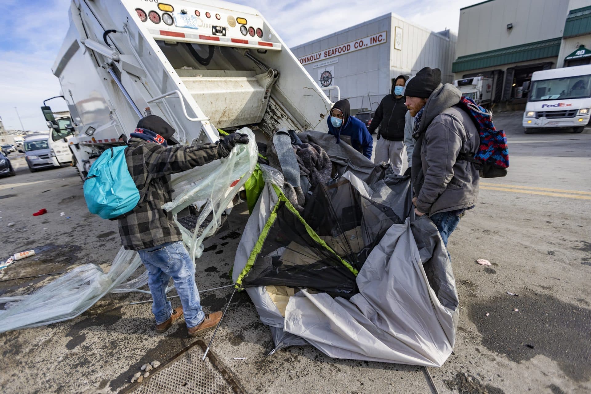 Volunteer shelter workers throw part of a tent and debris into a garbage truck at the Newmarket Triangle. (Jesse Costa/WBUR)