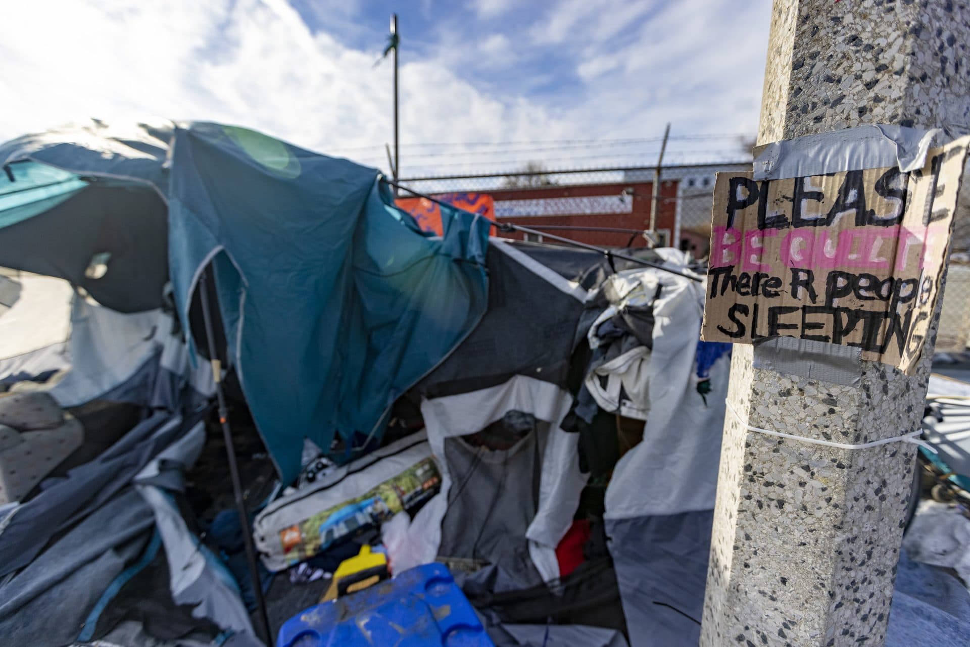 A sign that reads, “Please be quiet there R people sleeping” hangs on a lamp post in front of one of the last tents remaining in the homeless encampment at the Newmarket Triangle. (Jesse Costa/WBUR)