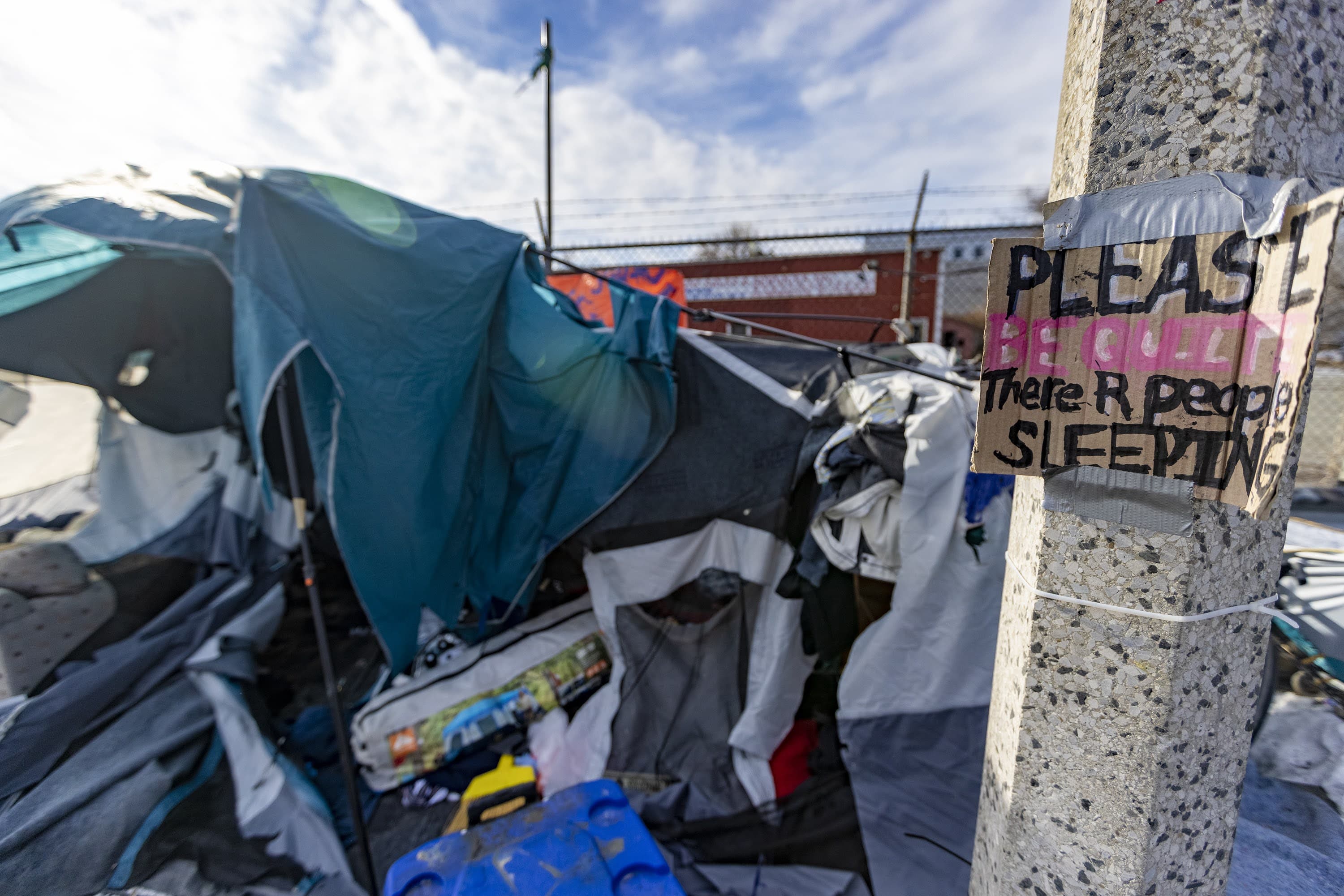 A sign that reads, “Please be quiet there R people sleeping” hangs on a lamp post in front of one of the last tents remaining in the homeless encampment at the Newmarket Triangle. (Jesse Costa/WBUR)