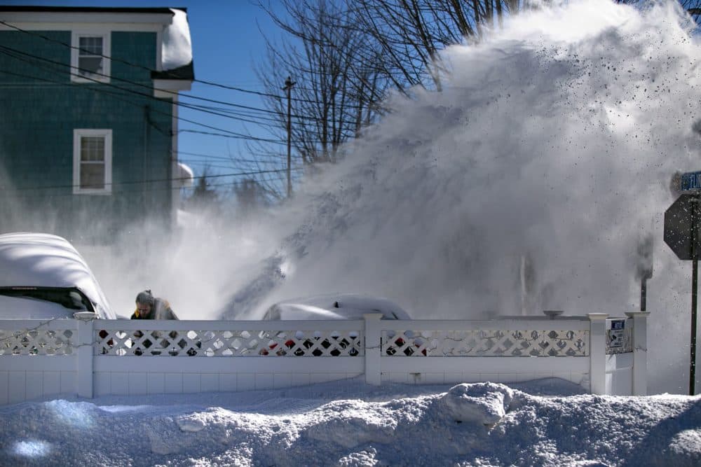 A man using a snowblower ducks to avoid the snow cloud being blown back at him by the wind on Flint Street in Somerville. (Jesse Costa/WBUR)