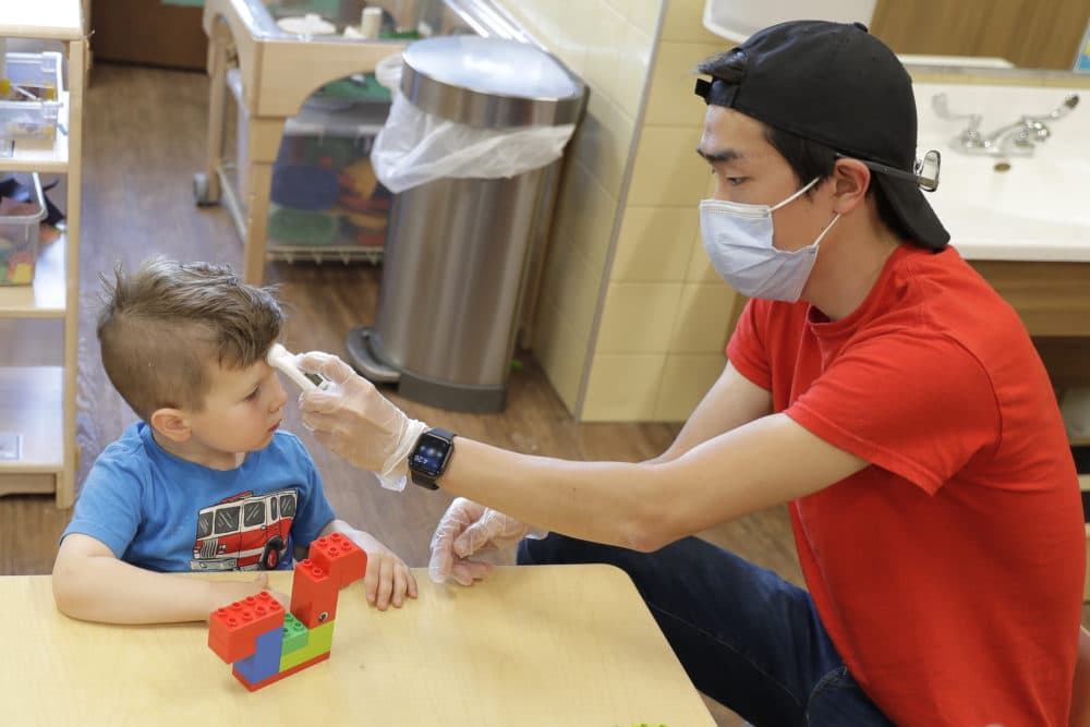 A teacher wears a mask as he takes a toddler's temperature. (Ted S. Warren/AP)