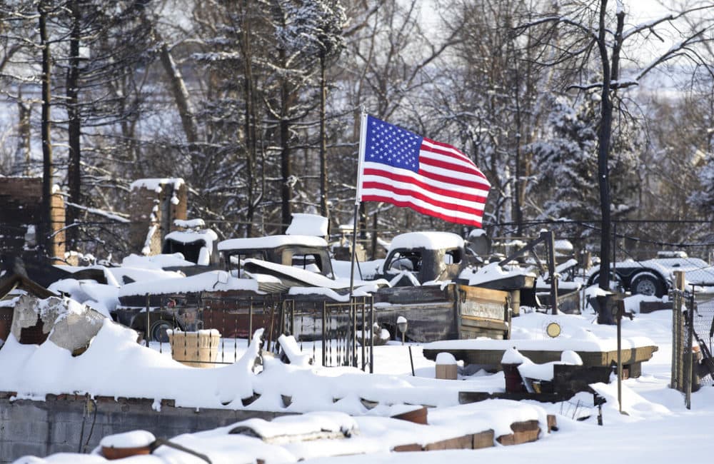 An American flag flutters in the wind over the charred remains of vehicles and a home destroyed by wildfires Thursday, Jan. 6, 2022, in Superior, Colo. (AP Photo/David Zalubowski)