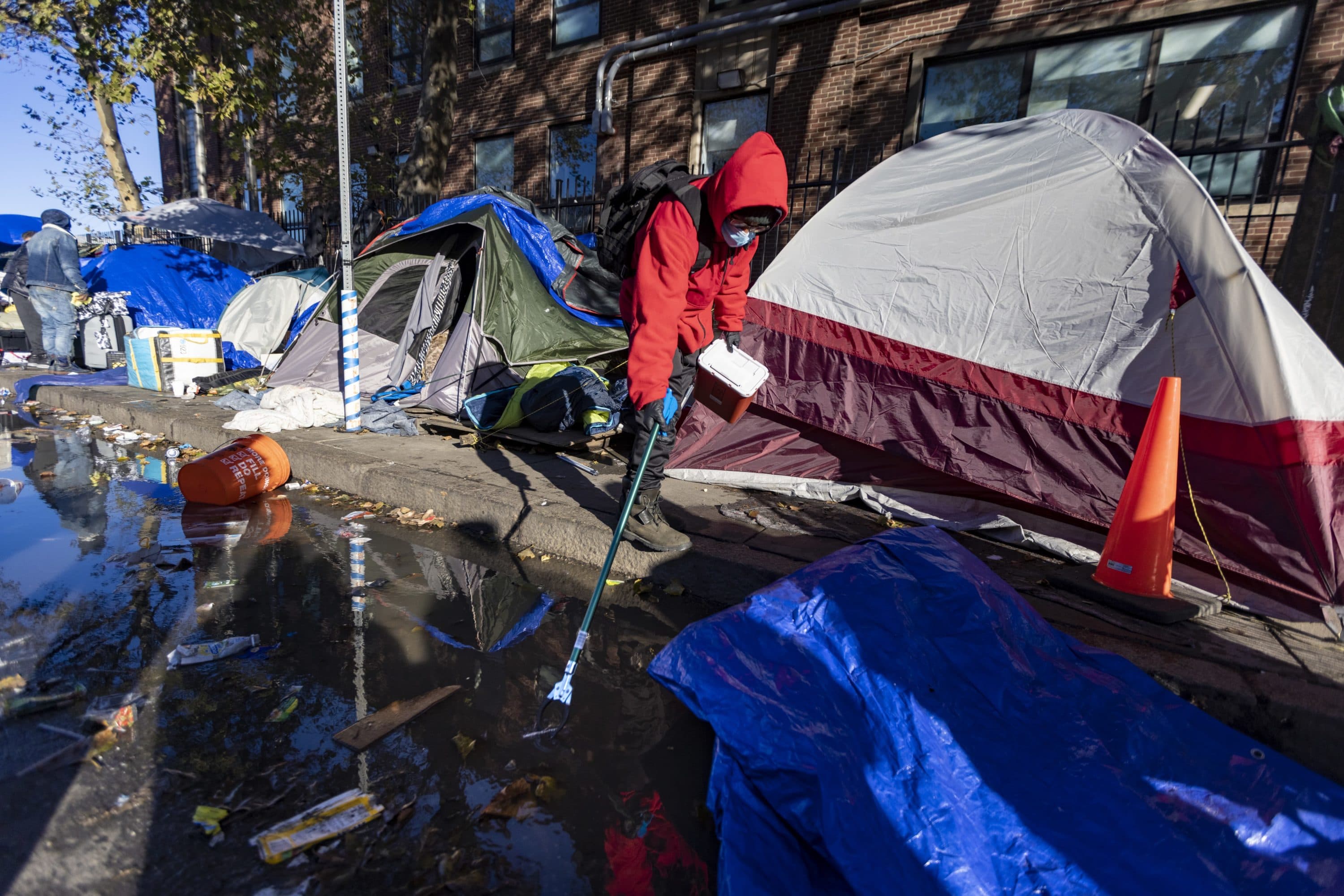A Boston Public Health Commission worker collects a syringe from a puddle on Southampton Street during the relocation of people living in tents in the "Mass and Cass" area late last year. (Jesse Costa/WBUR)