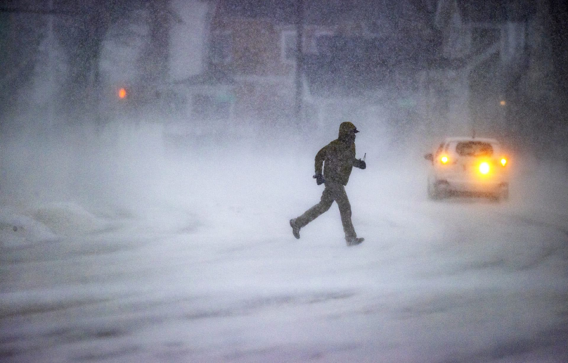 A man runs across Quincy Shore Drive as wind-blown snow creates visibility problems during the snowstorm in Quincy Saturday. (Stan Grossfeld/The Boston Globe via Getty Images)