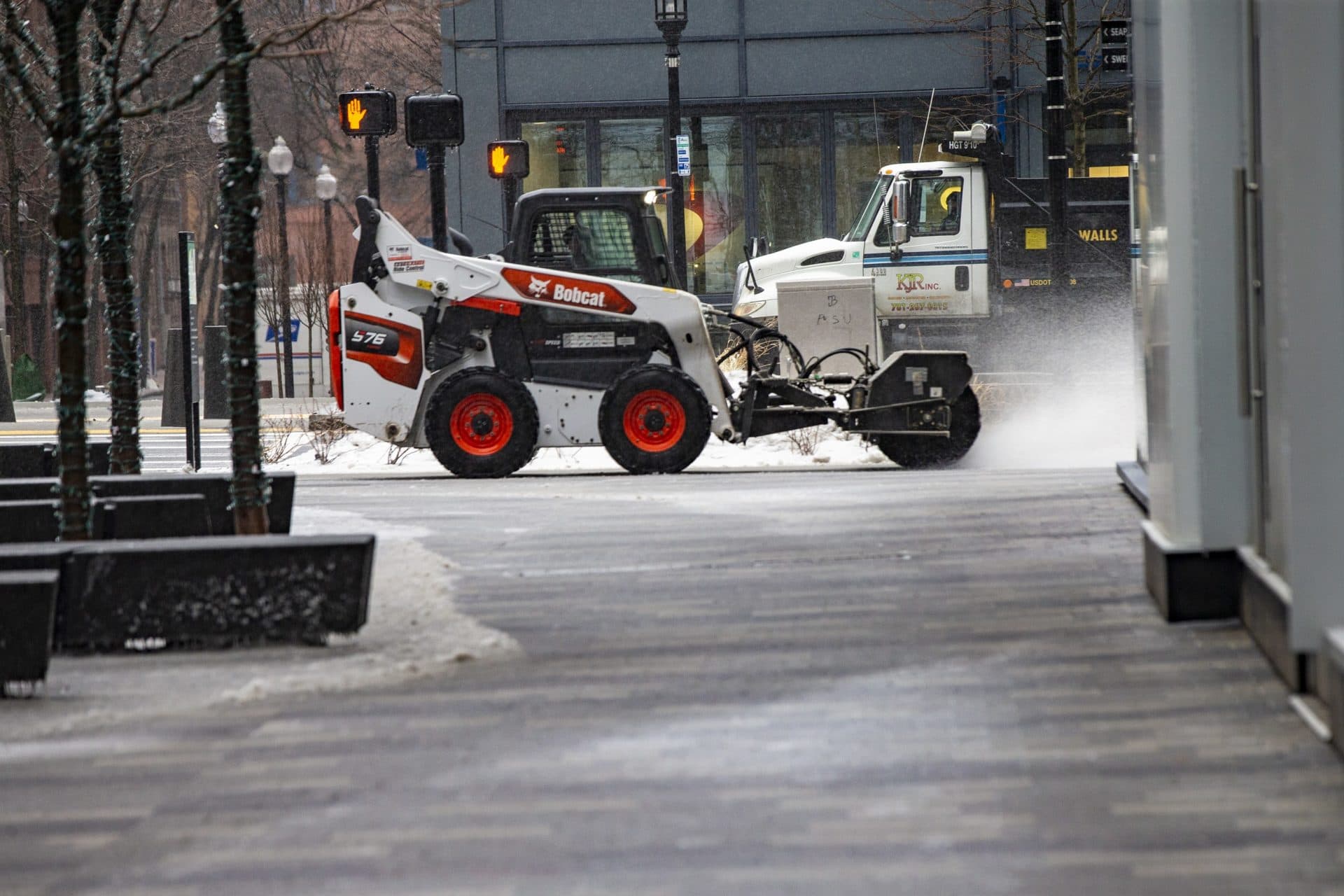 A worker driving a Bobcat, outfitted with a power broom, cleans up the sidewalk on Seaport Boulevard. (Jesse Costa/WBUR)