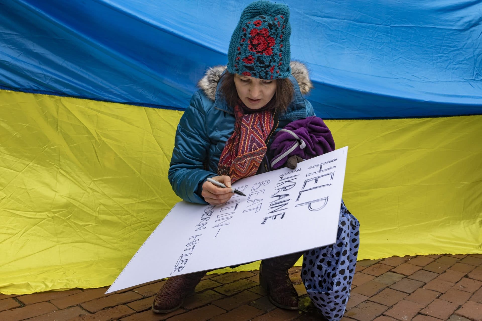 In front of the Ukrainian flag, Katya Fonrych, of Wayland, makes a sign that reads, “Help Ukraine Beat Putin-Modern Hitler,” at a rally to support Ukraine at the State House. (Jesse Costa/WBUR)